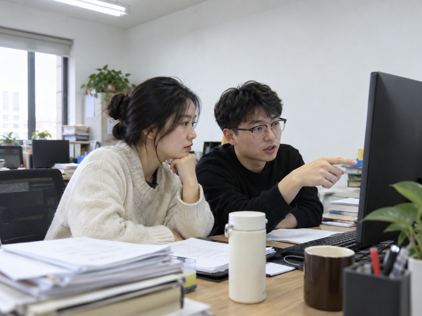 办公室里两位员工对着电脑讨论数据表格